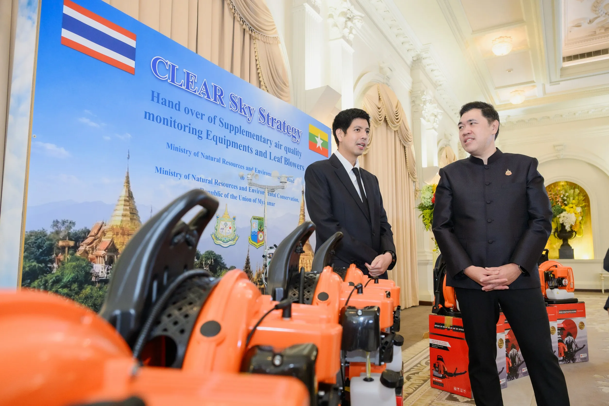 ภาพงานส่งมอบเครื่องเป่าลมและอุปกรณ์ตรวจวัดคุณภาพอากาศภายใต้ยุทธศาสตร์ "CLEAR Sky Strategy" โดยมีผู้แทนจากไทยและเมียนมายืนสนทนากันภายในห้องจัดงานที่มีป้ายประชาสัมพันธ์และธงชาติทั้งสองประเทศเป็นฉากหลัง
