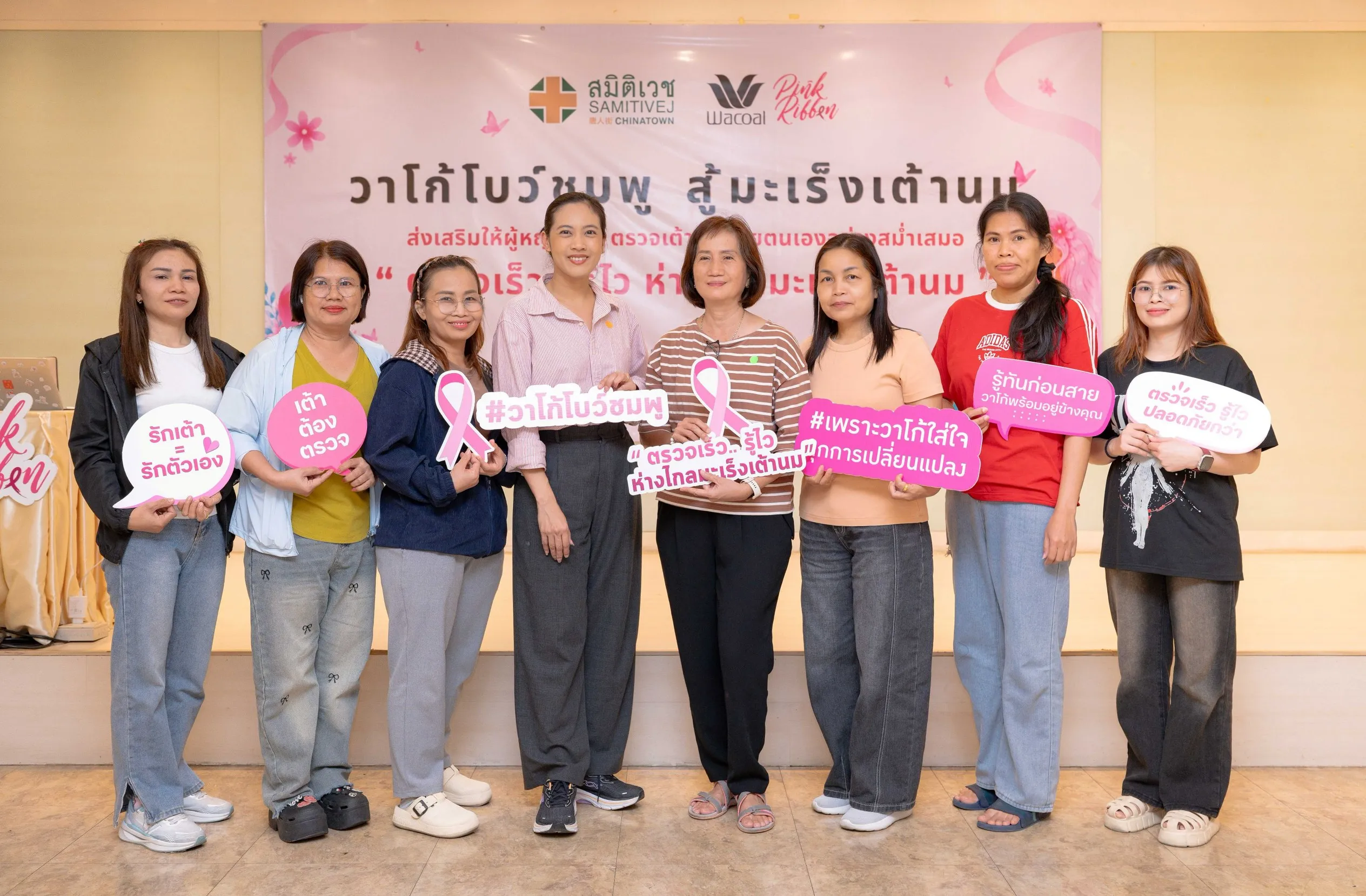 ภาพกลุ่มผู้หญิงแปดคนถือป้ายข้อความรณรงค์สีชมพูยืนถ่ายรูปร่วมกันหน้าแบนเนอร์กิจกรรม "วาโก้โบว์ชมพู สู้มะเร็งเต้านม" ซึ่งจัดโดยความร่วมมือของวาโก้และโรงพยาบาลสมิติเวช ไชน่าทาวน์