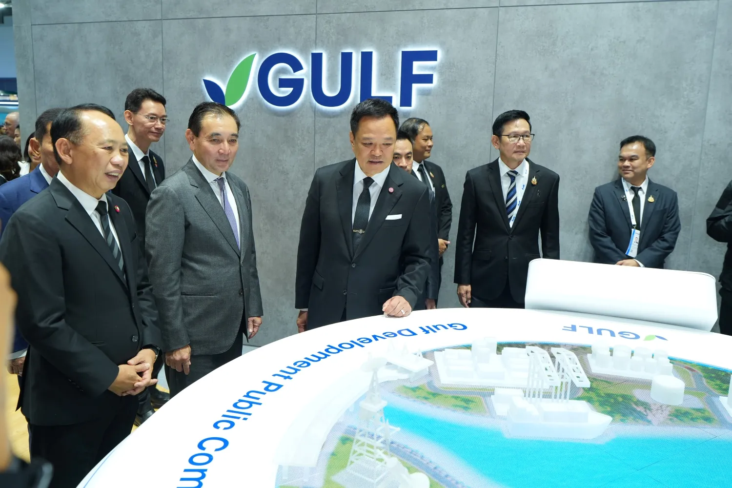 คณะผู้บริหารและเจ้าหน้าที่สวมชุดสูทยืนรวมกันหน้าโลโก้ GULF ขณะรับชมแบบจำลองโครงการพัฒนาโครงสร้างพื้นฐานบนหน้าจอแสดงผลในงานเปิดตัว Gastech 2026