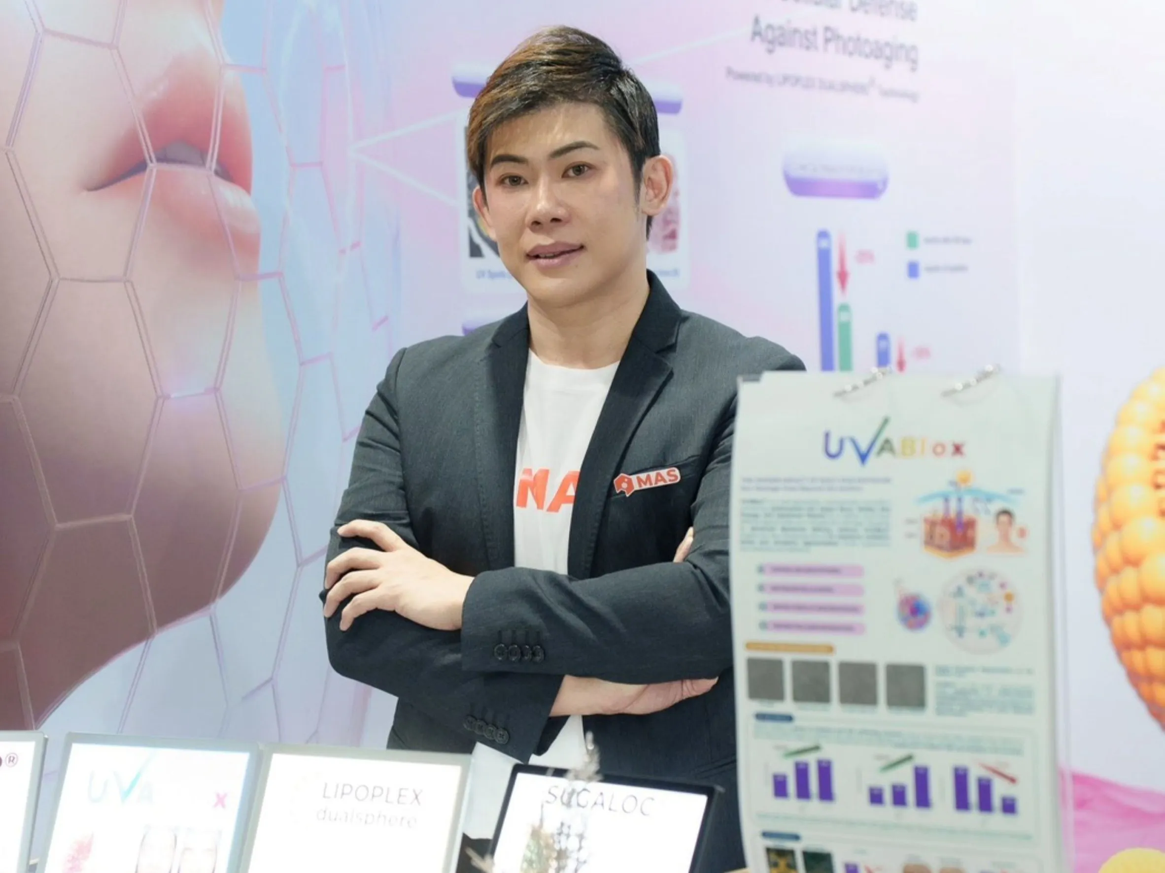 ผู้บริหารชายสวมสูทสีเทายืนกอดอกหน้าบูธแสดงนวัตกรรมความงาม UVABlox และผลิตภัณฑ์ Beauty-from-Within ของ MAS ในงาน Vitafoods Asia 2026