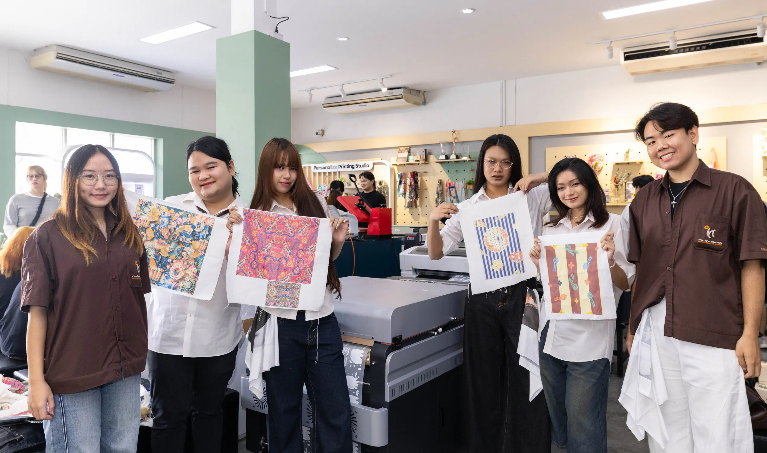 กลุ่มนักศึกษาดีไซเนอร์ไทยถือผลงานผ้าพิมพ์ลวดลายสีสันสดใสที่สร้างสรรค์จากเครื่องพิมพ์ผ้าดิจิทัลเอปสัน ยืนถ่ายภาพร่วมกันภายใน Persona Printing Studio ที่สยามเซ็นเตอร์