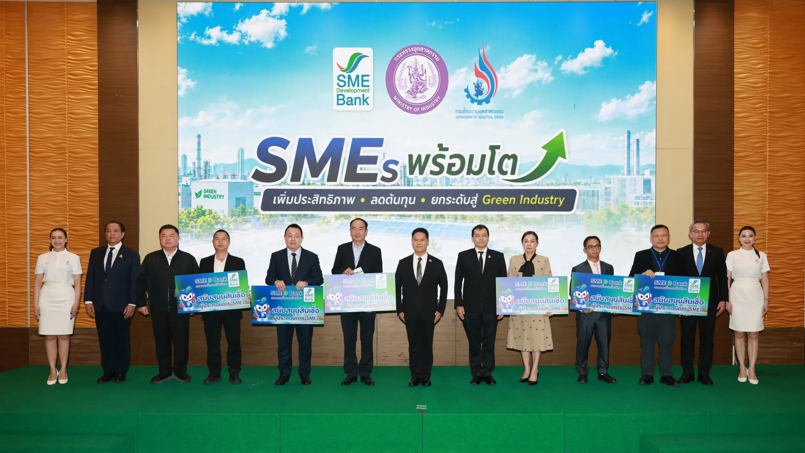 ผู้บริหาร SME D Bank และกรมโรงงานอุตสาหกรรมถ่ายภาพร่วมกับคณะผู้เกี่ยวข้องบนเวที พร้อมป้ายประชาสัมพันธ์โครงการสนับสนุนสินเชื่อผู้ประกอบการ SMEs สู่ Green Industry ในงานแถลงข่าว "SMEs พร้อมโต