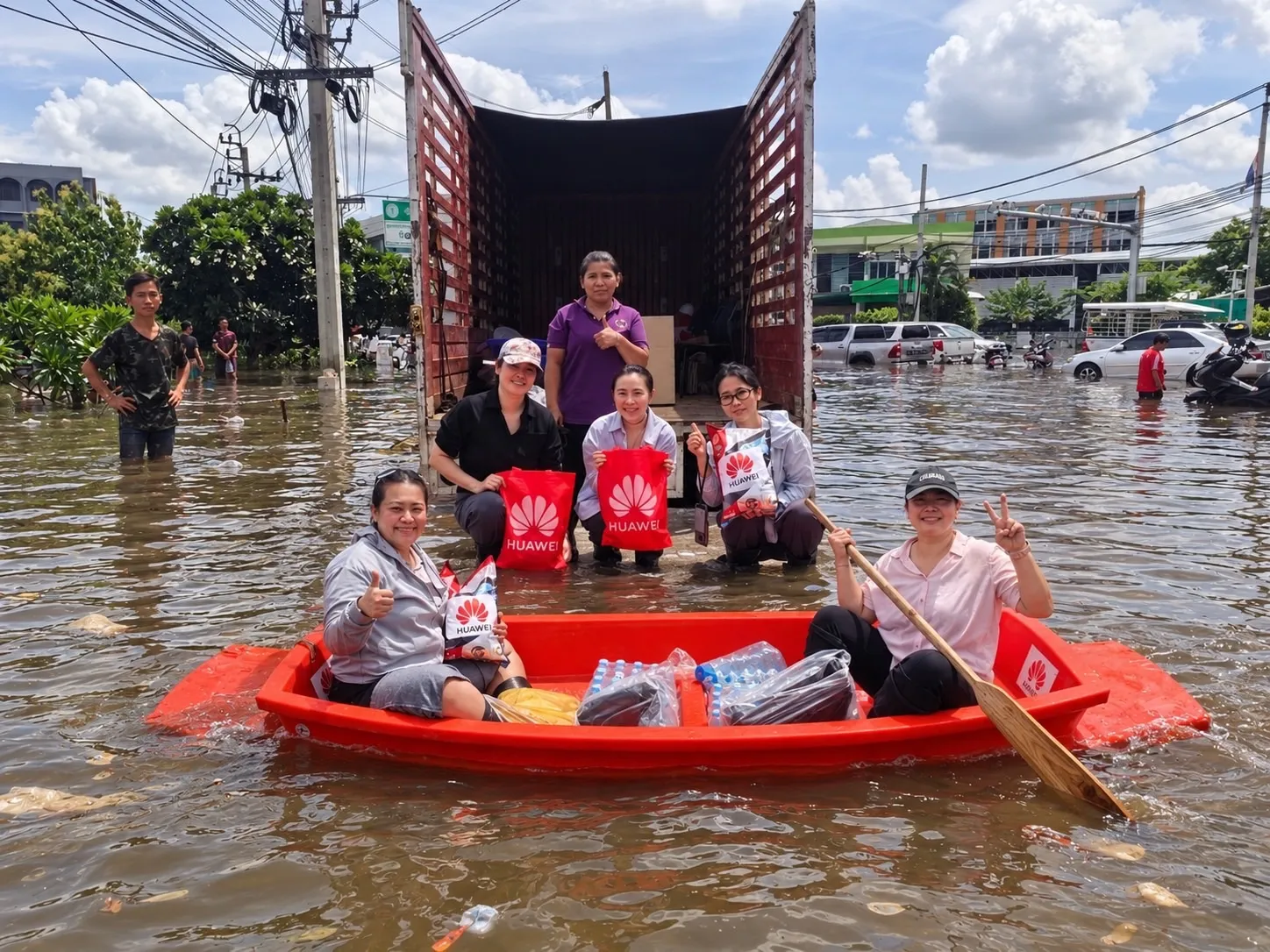 ทีมงานหัวเว่ยแจกถุงยังชีพและน้ำดื่มให้ประชาชนที่ประสบภัยน้ำท่วมในกรุงเทพฯ โดยใช้เรือพายลำเล็กสีส้มลำเลียงสิ่งของจากรถบรรทุกไปมอบให้ผู้ได้รับผลกระทบ