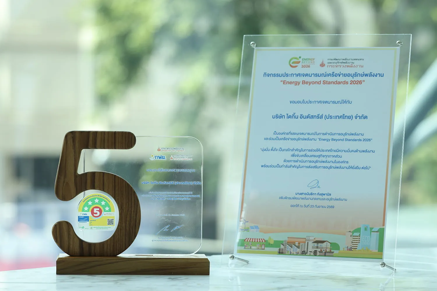 โล่รางวัลรูปเลข 5 พร้อมฉลากประหยัดพลังงานเบอร์ 5 และใบประกาศเจตนารมณ์เครือข่ายอนุรักษ์พลังงาน Energy Beyond Standards 2026 ที่มอบให้บริษัท ไดกิ้น อินดัสทรีส์ (ประเทศไทย) จำกัด ตั้งแสดงอยู่บนโต๊ะ