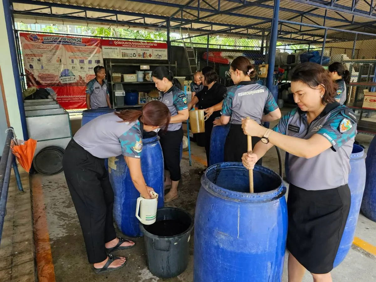 เจ้าหน้าที่กรมควบคุมมลพิษสวมเครื่องแบบสีเทาช่วยกันผลิตและตักน้ำหมักชีวภาพจากถังสีน้ำเงินขนาดใหญ่ใส่ภาชนะเพื่อแจกจ่ายช่วยเหลือพื้นที่ประสบภัยน้ำท่วม