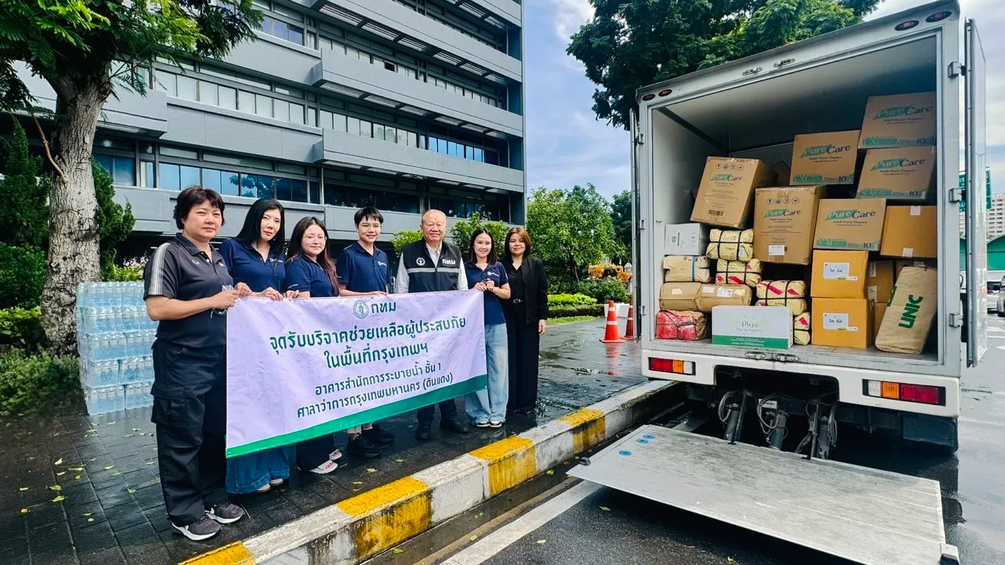 คณะผู้บริหารและพนักงานถือป้ายจุดรับบริจาคช่วยเหลือผู้ประสบภัยกรุงเทพมหานคร พร้อมมอบสิ่งของบรรเทาทุกข์และน้ำดื่มบรรจุขึ้นรถบรรทุกเพื่อส่งมอบความช่วยเหลือแก่ผู้ประสบอุทกภัย